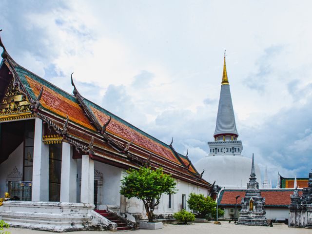 Monastery buildings with ornate pagoda roofs and white walls at Wat Phra Mahathat Woramahawihan in Thailand.