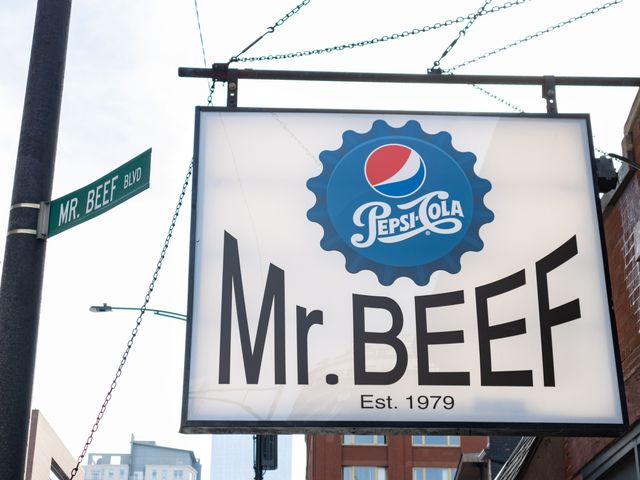 A street sign on the side of a brick building that reads Mr. Beef, est 1979 and a Pepsi-Cola logo.