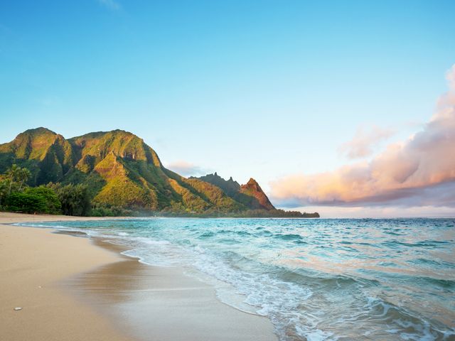 The lush green Hawaiian island of Kauai as seen from the beach with green mountains behind.