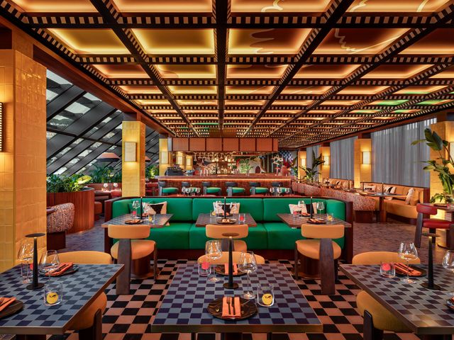 A modern looking restaurant with checkered detailing, lots of golden lighting, bright green couches and gold-tiled columns.