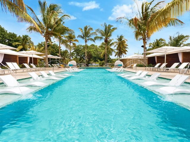 A pool with in-water white loungers on either side and fountains of water shooting across.