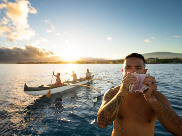 A man is seen blowing a conch shell next to others in an outrigger canoe during a sunrise canoe ride at Fairmont Orchid.