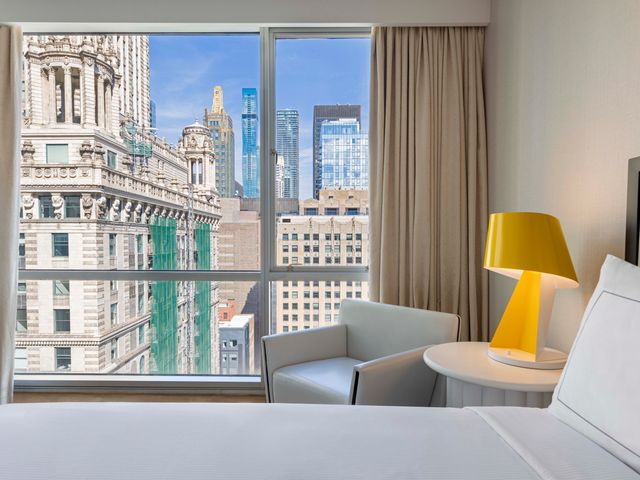 A hotel bed facing a window with urban city views at theWhit Chicago.