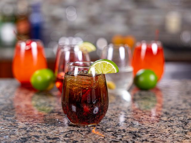 A dark soda-looking drink with a lime on the edge.
