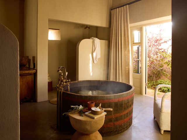 A barrel-style soaking tub with steaming water in the middle of a large bathroom inside a suite at Sterrekopje Farm.