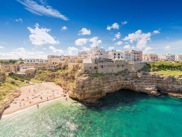 An aerial view over the turquoise waters, sandy beach, and craggy rocks in Polignano di Mare in Puglia.