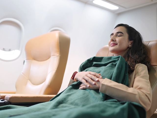 A woman sleeping on a plane holding onto a green blanket.
