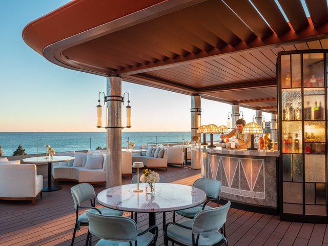 A mixologist makes a cocktail behind the bar at SEEN by Olivier with outdoor tables overlooking the Mediterranean sea