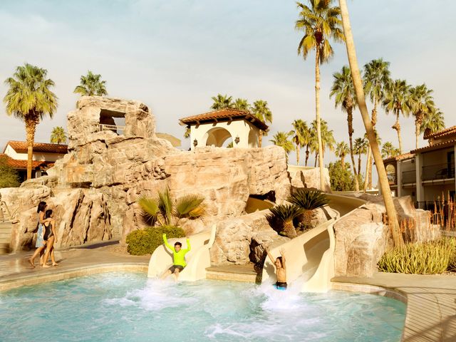 Water slides built into a rock formation with two people coming down and into the pool at Omni Rancho Las Palmas.