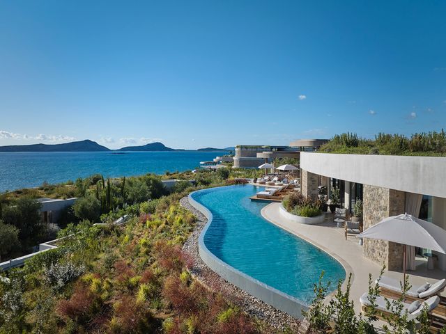 A villa with an infinity pool overlooking grassy hills and the ocean.