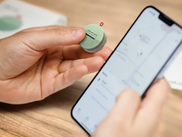 A hand holding a Roam Smart Tracker device next to a smartphone