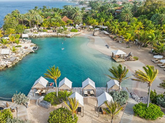 A tropical beach with palm trees, a protected cove, rocky areas, and cabanas and chairs.