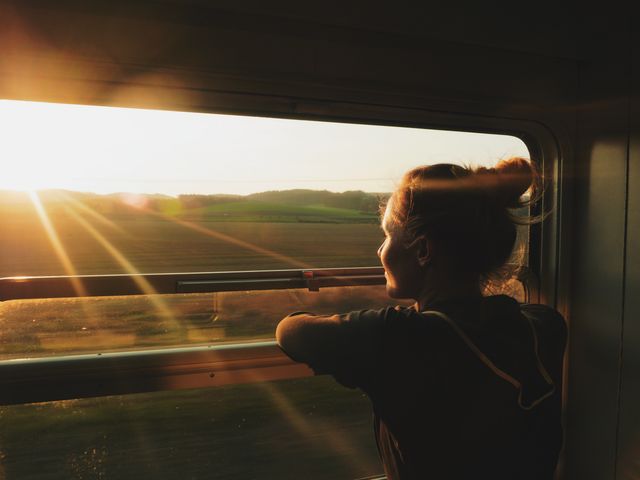 A woman looking out a train window at sunset.