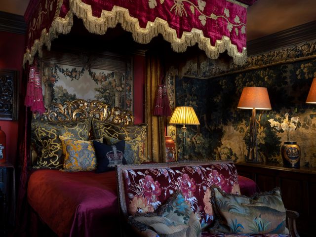 A regal, moody looking hotel room with a canopy bed, velvet upholstery, dark wallpaper, and lamps, at The Witchery.