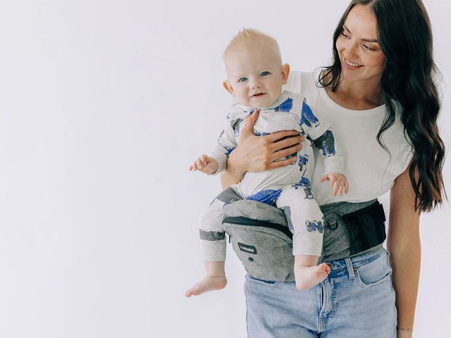 A woman holding her baby on a Tushbaby carrier.