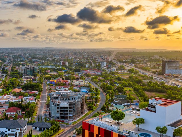 An aerial view of the skyline of Accra, Ghana at sunset with greenery and many low buildings.