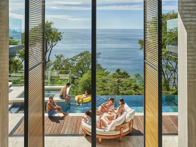 The view through a window of a family swimming in a private infinity pool at Four Seasons Resort Peninsula Papagayo, Costa Rica.