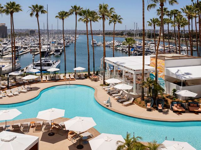A sprawling lagoon style pool surrounded by chairs, a restaurant, and a harbor filled with boats.