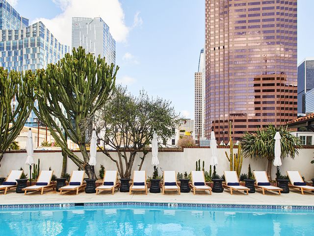 A pool lined with white chairs with views of the LA skyline at Hotel Figueroa.