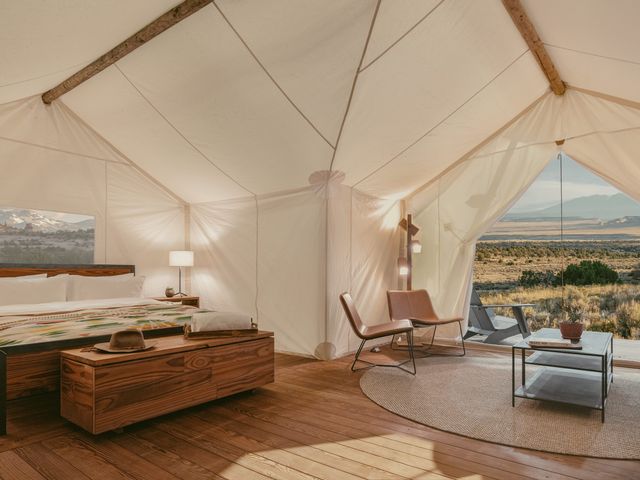 A tent with a large bed and seating area with the flaps open to reveal a desert landscape.