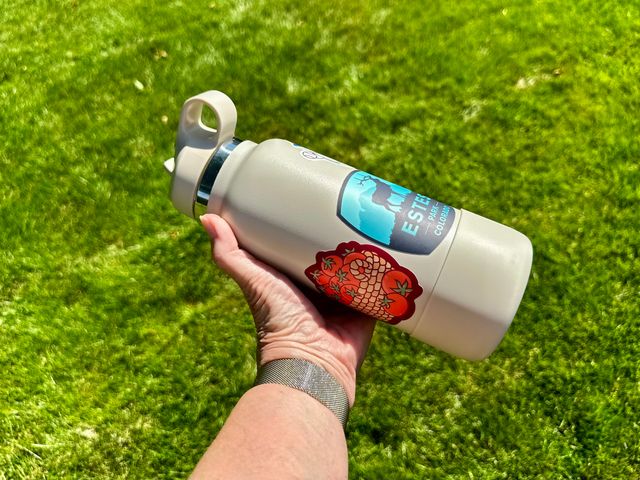 A hand holding a beige water bottle covered with two large stickers.