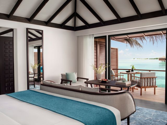 An overwater villa at Anantara Veli Maldives Resort with a large bed facing a patio on the ocean with a seating area.