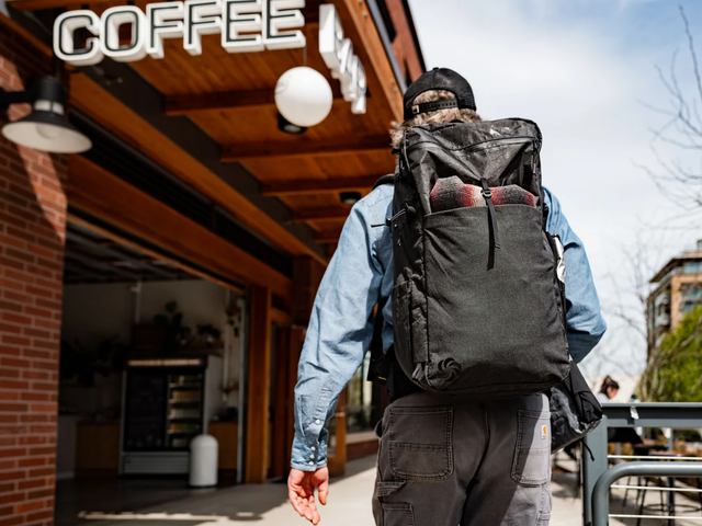 A man is seen from behind wearing a large backpack entering a coffee shop.