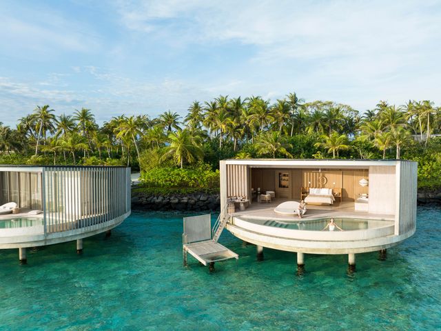 An overwater villa surrounded by lush palm trees at The Ritz-Carlton Maldives, Fari Islands.