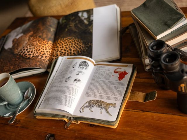 A desk with a notebook, binoculars, books, and coffee.