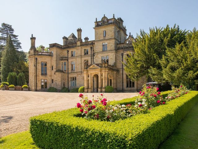 The stately entrance of Pale Hall framed by trees, bushes, and flowers.