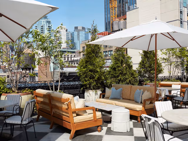 A plush rooftop area with lots of seating and umbrellas framed by the NYC skyline.