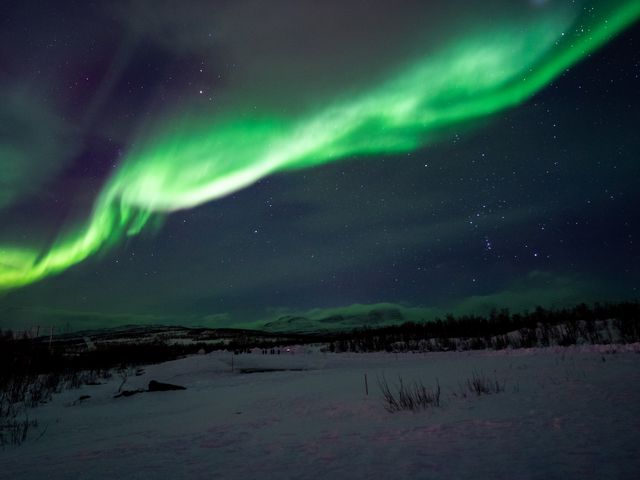 A strip of green northern lights seen in a night sky over a snowy landscape in Abisko, Sweden.