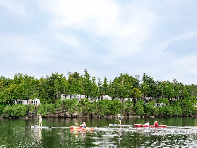 People kayak and paddleboard on the water with cabins located along the shore.
