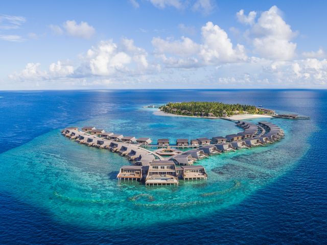 Overwater villas at The St. Regis Maldives Vommuli Resort sitting in a horseshoe in the water next to an island.