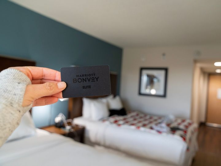 A hand holding a black Marriott Bonvoy card inside a hotel room.