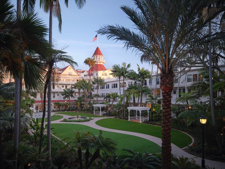 The Victorian Building at Hotel Del Coronado as seen through the middle of palm trees with a lush green lawn.