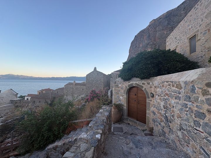 Stone walls and ocean views in Lower Town in Monemvasia with green bushes and pink flowers.