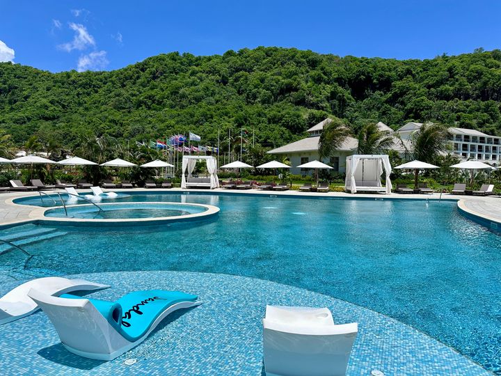 A sprawling lagoon-style turquoise pool with in-water chaise lounges, one of which says Sandals Resorts on it.