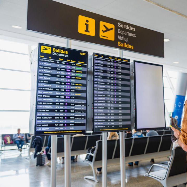 A male traveler stands and checks the flight departures board in an airport.
