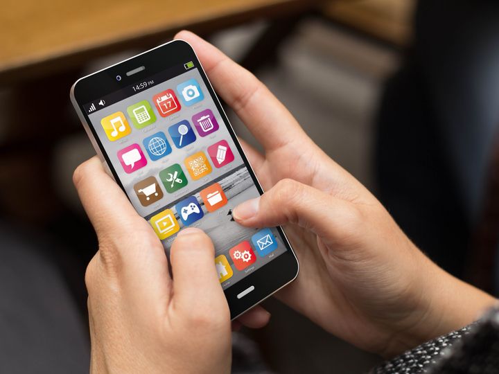 Hands holding a smartphone with apps showing.