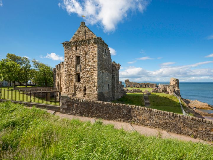 The ruins of St. Andrews Castle in Scotland next to the sea under a blue sky.