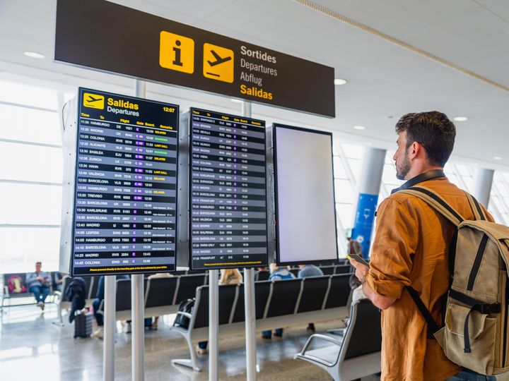 A male traveler stands and checks the flight departures board in an airport.