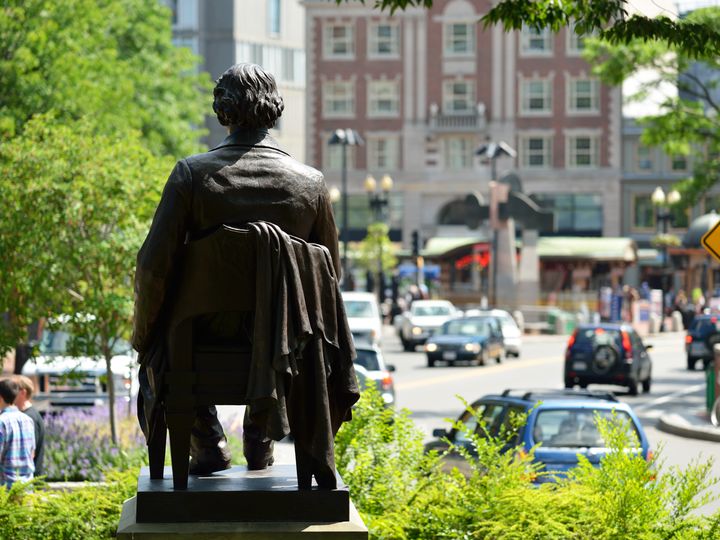 John Harvard Statue in Harvard Square as seen overlooking traffic and buildings.
