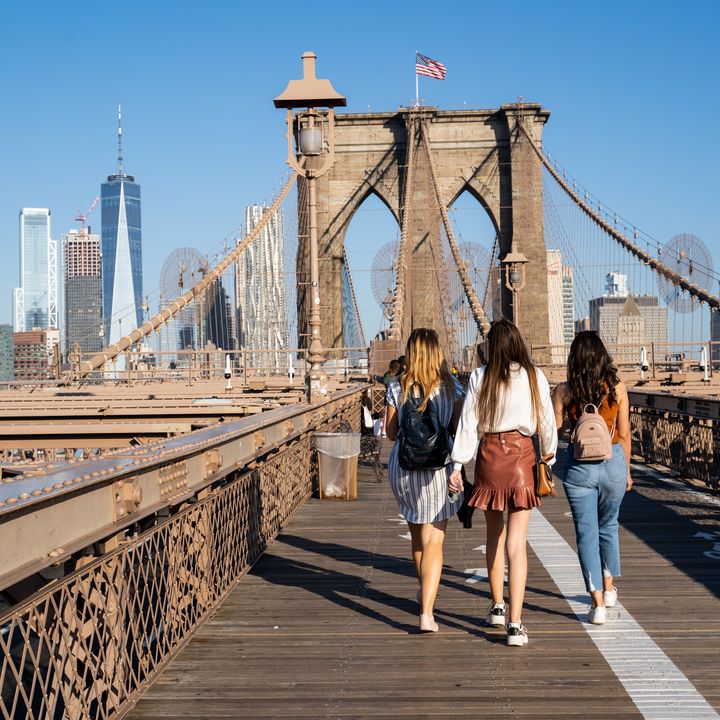 Teenagers walk over the Brooklyn Bridge as seen from behind.
