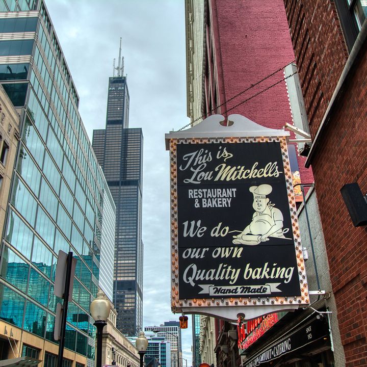 A sign on the side of a brick building on an urban street that says, “This is Lou Mitchell’s Restaurant and Bakery. We do our own quality baking.”