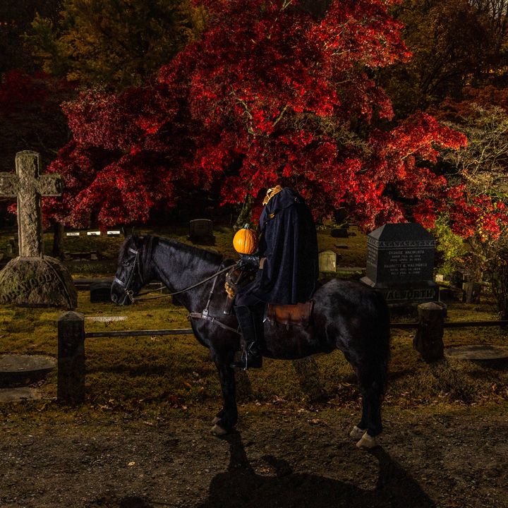 A black horse with what looks like a headless rider on top in the Sleepy Hollow Cemetery at night in fall.