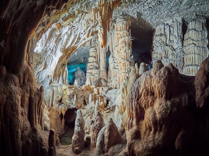 A view of stalactites and stalagmites in an underground cavern that’s partially lit up and dark in other places.