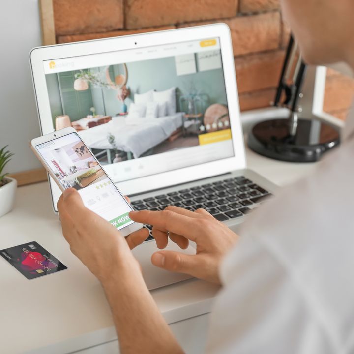 A person is seen booking a hotel room on a laptop while holding a mobile next to a credit card.