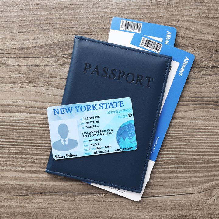 A card that says it’s a New York State ID is placed on top of a passport case that contains what appear to be two plane tickets.