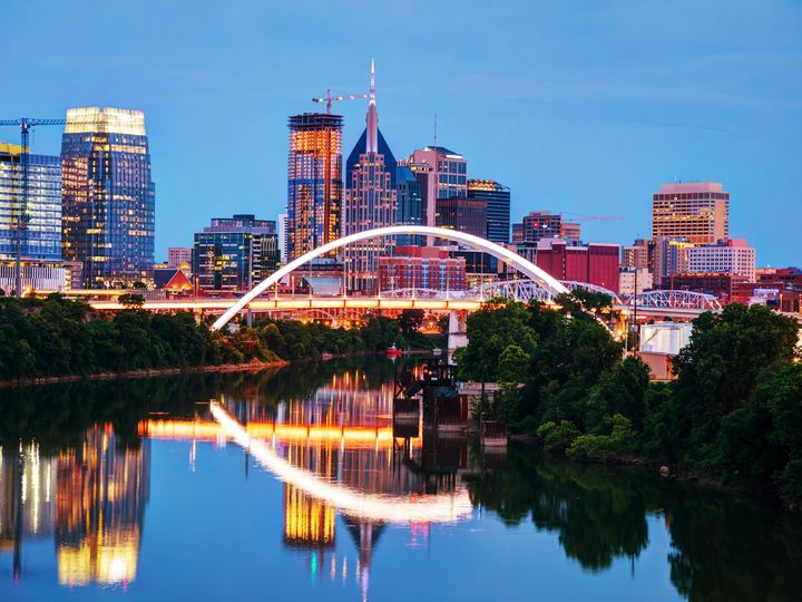 The Nashville skyline at night as seen from the river with the buildings and bridge lit up.